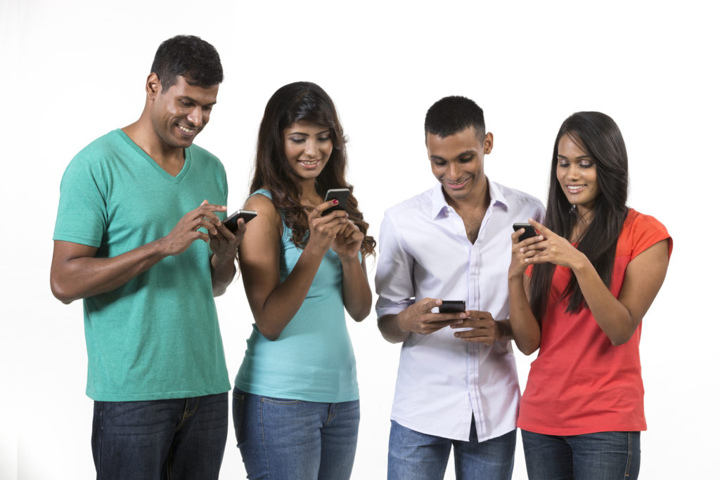 Group of young Indian friends using their smartphones. Happy Asian people using their cell phones. Isolated on white background.
